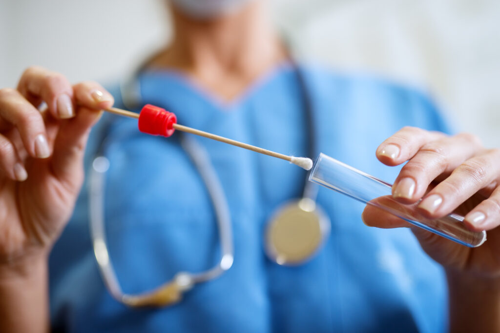 Close up of a female clinician's hands holding cotton swab and test tube.